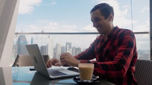 Happy Businessman Sitting Cafe Using Laptop Finishes Project and Wins Big on Background of Big City Skyscrapers. Makes Successful Gestures Raises Arms in Celebration. Gesture yes. — Stok video