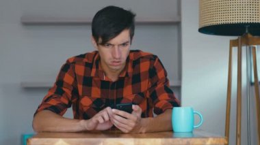 Angry Man Using Mobile phone at home. Frustrated entrepreneur is angry with the message that he read in the smartphone. Stressed businessman uses smartphone.