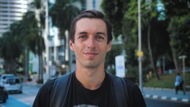 Portret van knappe jonge man toerist met een rugzak kijkend naar de camera in de grote stad. Stedelijke achtergrond. — Stockvideo