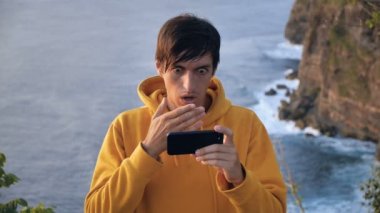 Gezgin Adam 'ın Smartphone' da kaybına tepkisi şok oldu. Nahoş bir şekilde şaşırmış ve korkmuştu. Arka plandaki deniz dalgalarının üzerindeki uçurum
