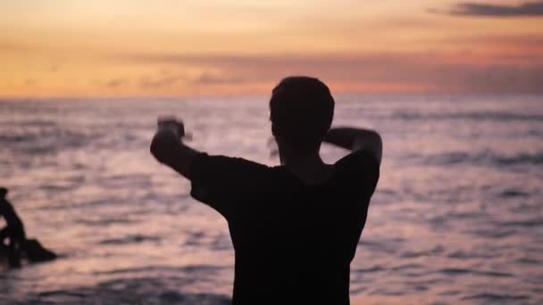 Silhouette dell'uomo alza le mani in piedi di nuovo sulla bella spiaggia tropicale sul tramonto rosso. Concetto di libertà . — Video Stock