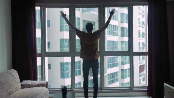 Sylwetka młodego człowieka patrzącego przez okno pokoju i podnoszącego ręce do góry. Koncepcja marzeń i sukcesu. — Wideo stockowe