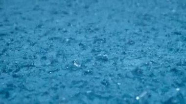 Yakın çekim yağmur, yağmur damlaları yavaş çekimde büyük bir su birikintisine düşüyor. Yağmur mevsimi.