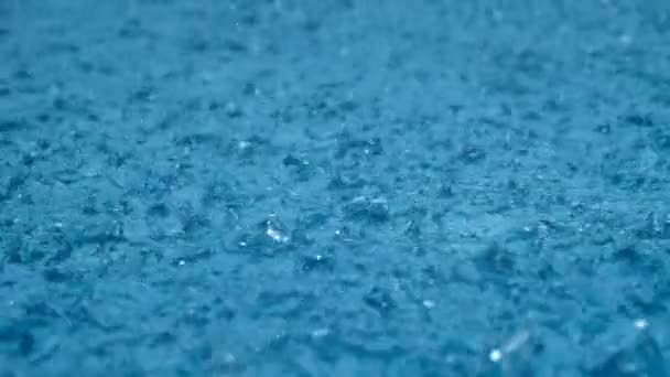 Közelről eső, esőcseppek hullanak egy nagy pocsolyába lassított felvételen. Esőidény. — Stock videók