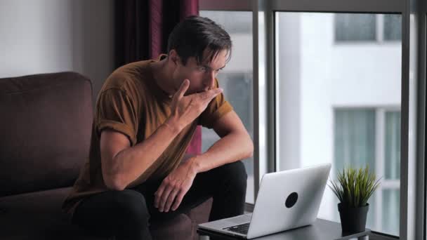 Bang man is geschokt en onaangenaam verrast door wat hij zag in de laptop tijdens het zitten aan tafel thuis — Stockvideo