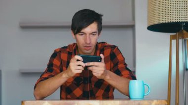 Young man using mobile phone playing video games at home. Male shows different emotions during the game.