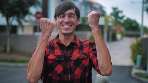 Expressive Young Man Showing Yes Winner Gesture. Happy amazed handsome male in plaid shirt standing rejoicing and celebrating his victory outside at urban city background — ストック動画