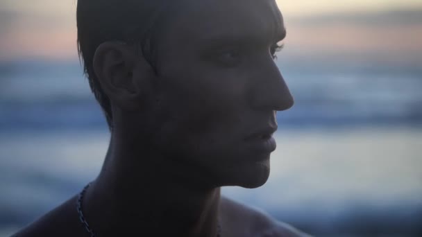 Retrato close-up de um jovem caucasiano desfrutando de tempo livre em uma praia junto ao mar ao pôr do sol na noite — Vídeo de Stock