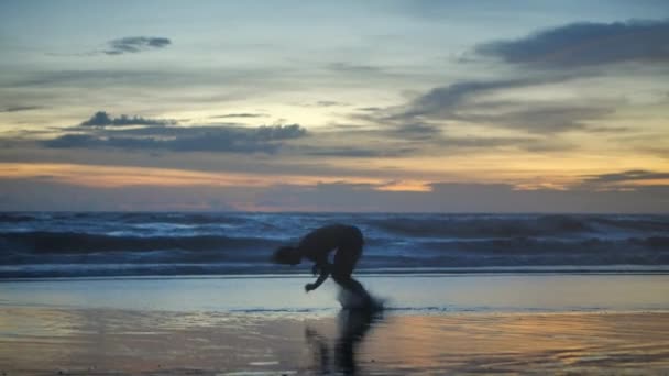 Silhouette Athlète homme pratiquant l'entraînement sur la plage au coucher du soleil. L'athlète fait un saut périlleux dans le dos et fait des pompes sur fond d'océan et de coucher de soleil . — Video