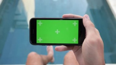 Close-up of smartphone with Green Screen Sitting at home near pool , holding by man in Horizontal Mode, watching movie on touch screen with Tracking Markers.