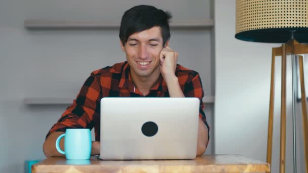 Retrato de homem bonito sorrindo usando laptop. Freelancer gosta de trabalhar no computador em casa e beber café . — Vídeo de Stock