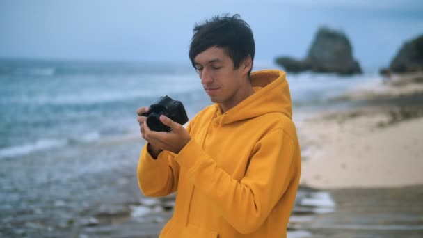 Mężczyzna fotograf w żółtej bluzie robi zdjęcie na pięknej dzikiej tropikalnej plaży wieczorem — Wideo stockowe