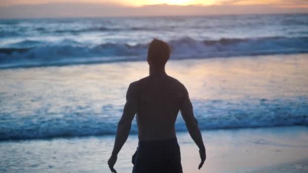 Silhouet van een gespierde man steekt zijn handen op en mediteert op zonsondergang zee op de achtergrond. — Stockvideo