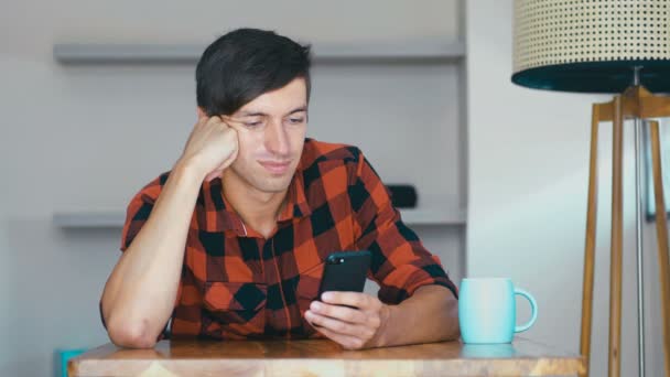 Homem alegre está usando smartphone se divertindo sorrindo em casa sozinho relaxando em casa — Vídeo de Stock