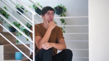 Pensive sad and depressed young man sitting alone on stairs at home: painful sad man.