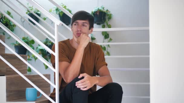 Pensativo triste y deprimido joven sentado solo en las escaleras en casa: hombre triste doloroso . — Vídeo de stock