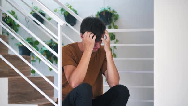 Pensativo triste y deprimido joven sentado solo en las escaleras en casa: hombre triste doloroso . — Vídeos de Stock