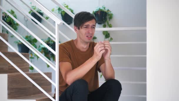 Smutný muž brečí doma, sedí na schodech. — Stock video