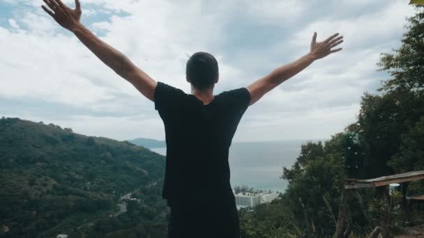 Jonge man reiziger steekt zijn handen hoog op de top van de berg boven prachtig landschap — Stockvideo