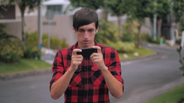 Jovem segurando smartphone jogar jogo móvel ao ar livre na rua da cidade, jovem feliz usando estudo de trabalho aplicativo de mídia social no telefone celular olhando para a tela — Vídeo de Stock