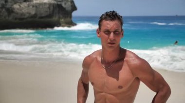 Yakışıklı genç adamın portresi, iyi eğitimli kaslı atlet, güzel kumsalda poz veriyor.
