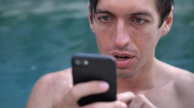 Yüzme havuzunda akıllı telefon kullanarak tatilde gülümseyen genç adama yakın plan.