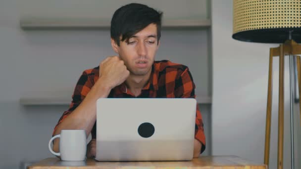 Unatkozó fiatalember szörfözik és cseveg. Fáradt szabadúszó dolgozik laptop otthon. — Stock videók