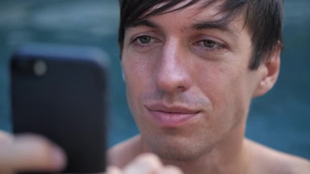 Close-up de sorrir jovem em férias usando smartphone em uma piscina — Vídeo de Stock