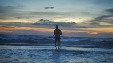 Silhouette of muscular man with a naked torso walking on the beach at sunset.