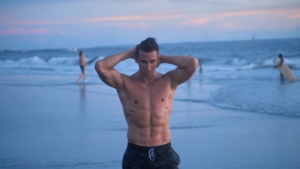 Retrato de un hombre musculoso con un torso desnudo en la playa al atardecer . — Vídeos de Stock
