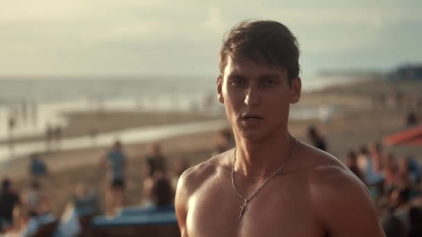 Retrato de un hombre musculoso guapo con un torso desnudo en la playa al atardecer . — Vídeos de Stock