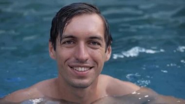 Mutlu gülümseyen bir adamın yakından çekilmiş portresi havuzda keyif çatıyor.