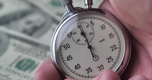 Nahaufnahme einer Person, die eine Stoppuhr auf Geld-Dollar-Hintergrund hochfährt. Zeit ist Geld. Fristkonzept. — Stockvideo