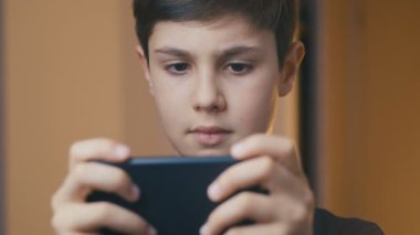 Genç çocuk akıllı telefonuyla oynuyor. Akıllı telefonda cep telefonu oyunu oynayan bir çocuk. Evde video oyunu oynayan çocuk