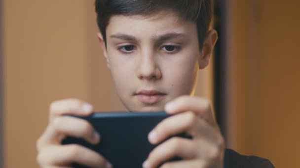 Niño jugando en su teléfono inteligente. Niño jugando juego móvil en el teléfono inteligente. Niño jugando videojuego en casa — Vídeos de Stock