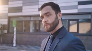 Modern ofis binasının yanında duran yakışıklı sakallı takım elbiseli iş adamı.