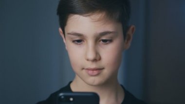 Genç çocuk akıllı telefonuyla oynuyor. Akıllı telefonda cep telefonu oyunu oynayan bir çocuk. Evde video oyunu oynayan çocuk