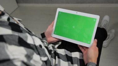 Sandalyede oturan adam yeşil ekran krom anahtarlı dijital tablete bakıyor.