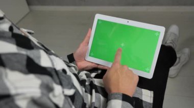 Sandalyede oturan adam yeşil ekran krom anahtarlı dijital tablete bakıyor.