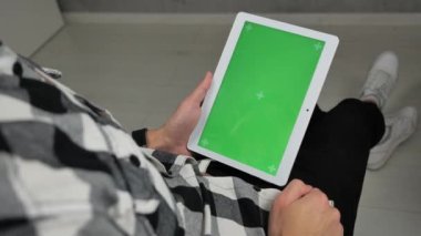 Sandalyede oturan adam yeşil ekran krom anahtarlı dijital tablete bakıyor.