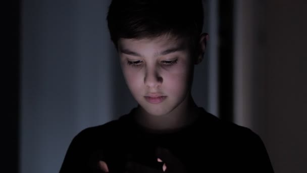 Plan de nuit d'un garçon de 11 ans utilisant un smartphone. Lumière réflexion sur le visage mignon jeune garçon . — Video
