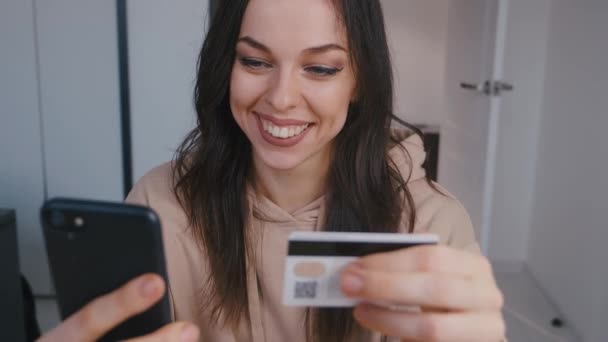 İnternetten alışveriş yapan genç bir kadın. Çevrimiçi gülümseyen kadın internet üzerinden akıllı telefon alışverişi yapıyor ve ev hayatı tarzında kredi kartı kullanıyor. Dijital aygıt kullanarak kolay ödeme. — Stok video