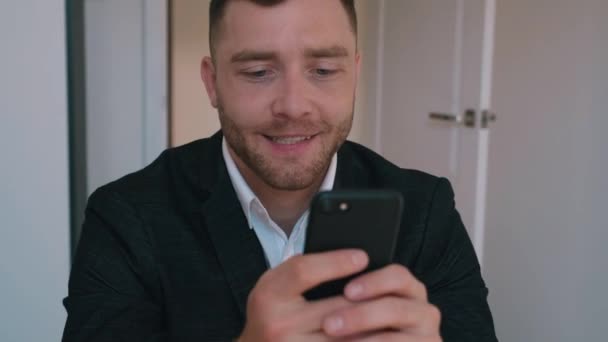 Homme d'affaires confiant en costume formel assis à son bureau au bureau à domicile à l'aide d'un téléphone intelligent, naviguant sur Internet, les médias sociaux . — Video