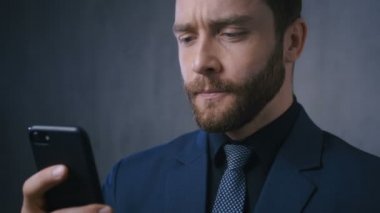 Kendine güveni tam bir iş adamı akıllı telefonuna bakıyor ve zafer jesti yapıyor. Başarılı erkek girişimci akıllı telefona bakarak başarıyı kutluyor