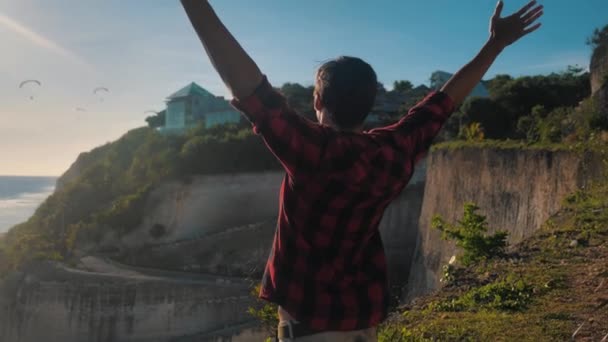 Joven viajero levantando sus manos en lo alto de la montaña por encima de hermoso paisaje en la puesta del sol de oro — Vídeo de stock