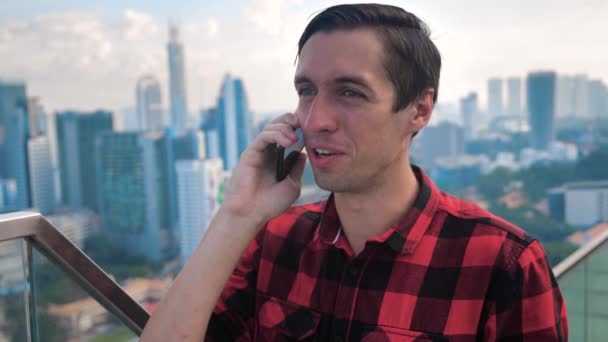 Jongeman met Smartphone die buiten in de stad staat en een telefoontje pleegt. Skyscraper Gebouwen op achtergrond. — Stockvideo