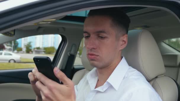 おびえた男が車の後ろに座ってスマートフォンを使っている。彼は悪い知らせを受けた。ショックを受けた実業家. — ストック動画