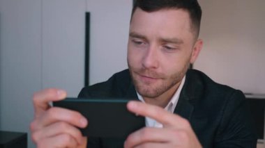 Yakışıklı iş adamı evde oturmuş akıllı telefondan video izliyor.