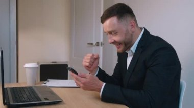 Heyecanlı iş adamı kazananın elinde akıllı telefon var. İnternet haberlerini okuyun. İnternet üzerinden bahis oyununa hayran kalmışsınız.
