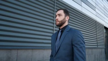 Kendine güvenen iş adamı işe gidip geliyor. Takım elbiseli genç adam caddede ofis binasının yanında yürüyor.